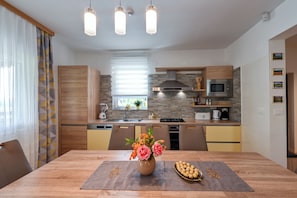 A modern kitchen with a dining area, featuring a central island with a vase of flowers and chocolates, a built-in microwave, and a stove.