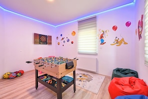 A room with a foosball table, a dartboard, and wall decorations including planets and cartoon characters.