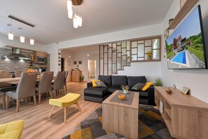 Ein modernes Wohnzimmer mit Sofa, Sesseln, einem Couchtisch und einem Essbereich mit Tisch und Stühlen.