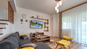 A modern living room with a grey sofa, yellow ottoman, and a flat-screen TV mounted on the wall. - Spacious villa in Zagorje with jacuzzi, sauna, pool, barbecue, and scenic views (Pregrada)