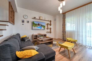 Ein modernes Wohnzimmer mit einem grauen Sofa, einem gelben Ottomanen und einem an der Wand befestigten Flachbildfernseher.