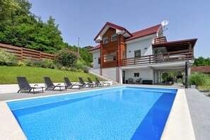 Ein modernes, zweistöckiges Haus mit Swimmingpool, Sitzgelegenheit im Freien und Satellitenschüssel.