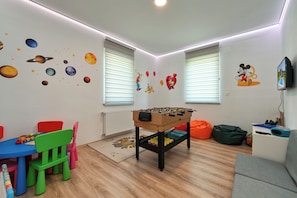 A room with a foosball table, colorful chairs, a sofa, and a television on the wall.
