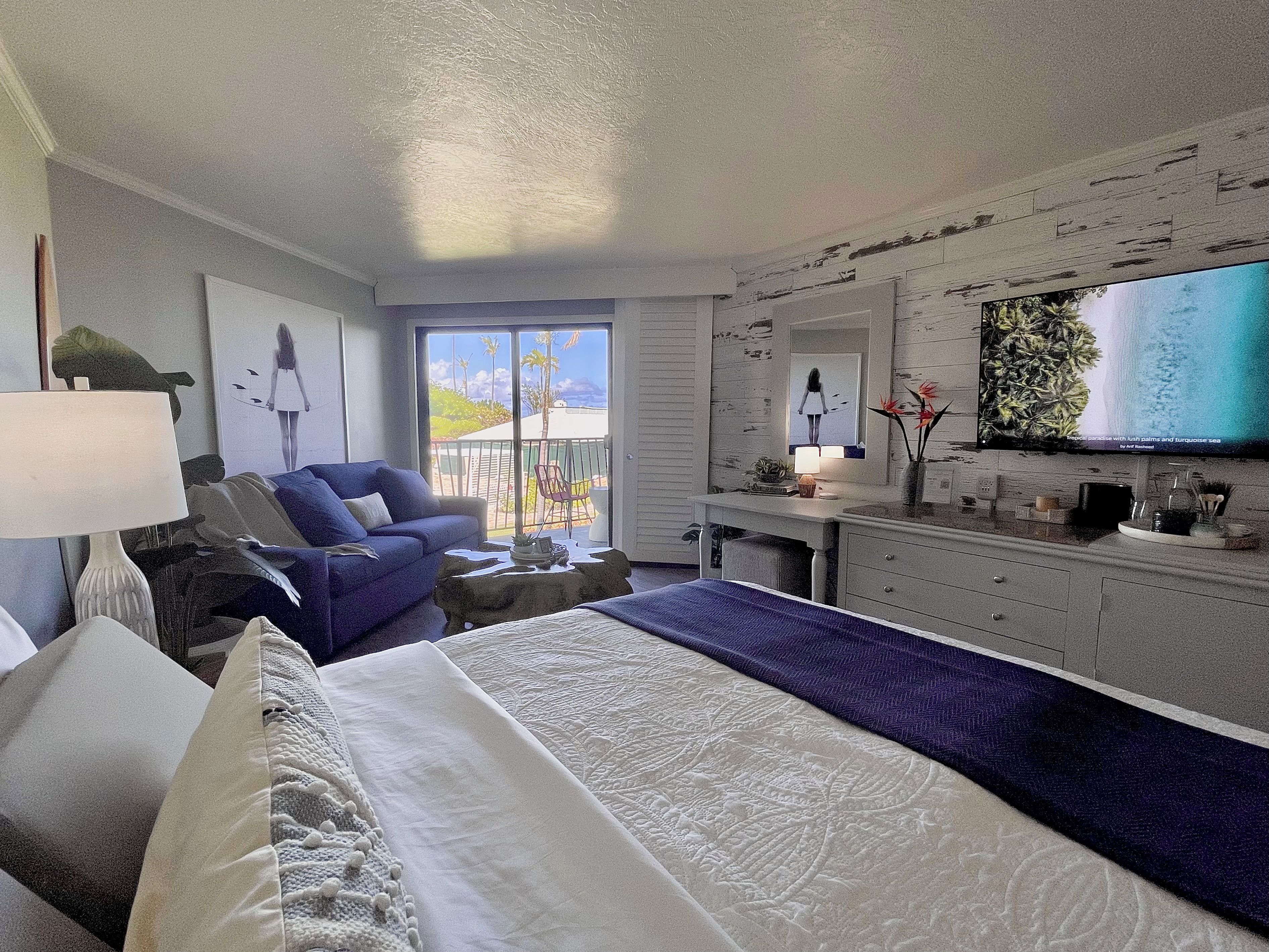 A hotel room with a bed, a chair, a desk, a television, and a balcony with a view.