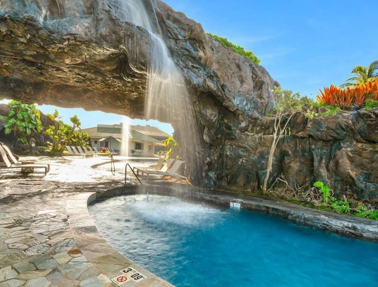 Ein Pool mit Wasserfall, umgeben von Liegestühlen und einer Steindeck.