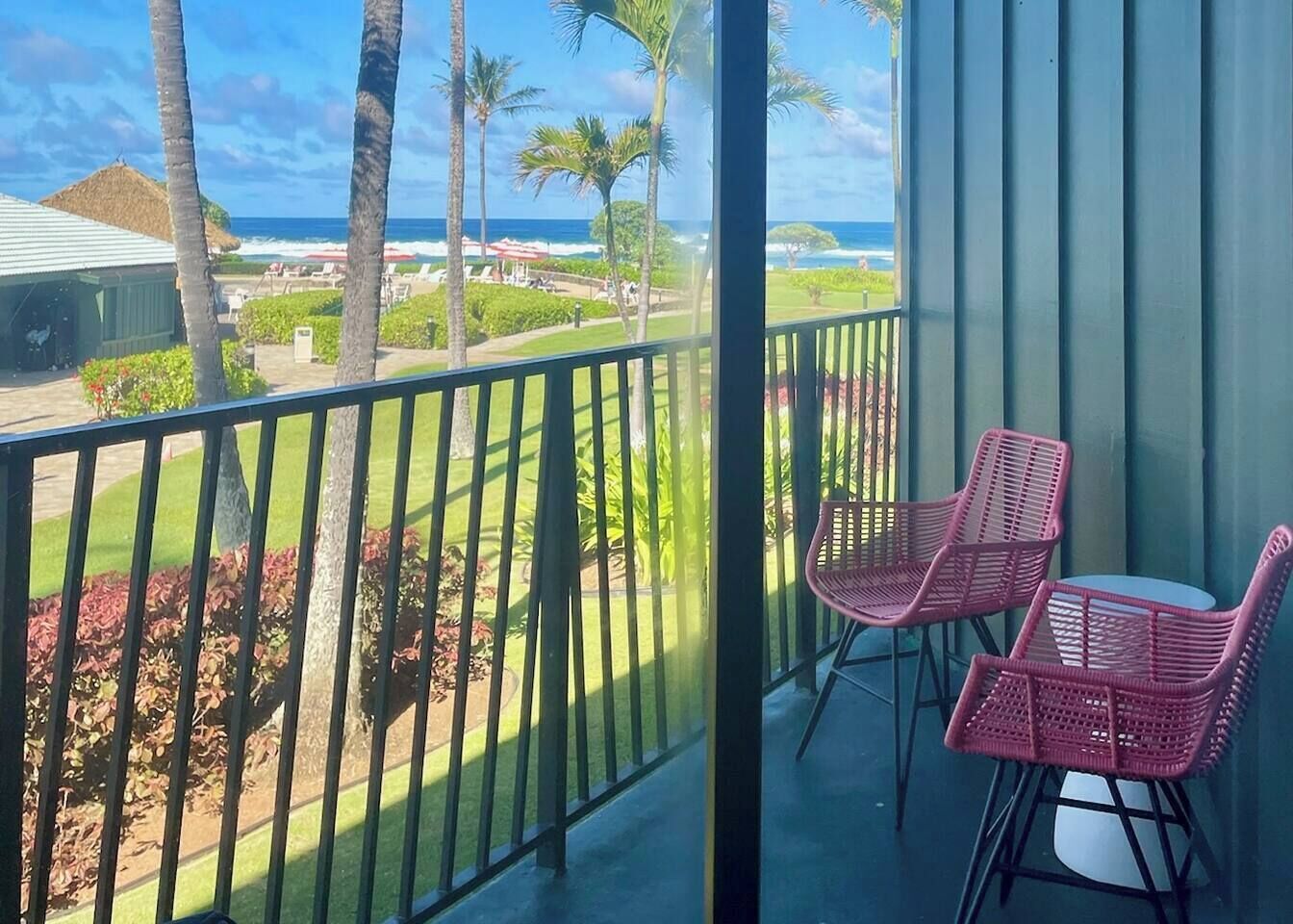 En balkon med udsigt over havet, palmer og en græsplæne.