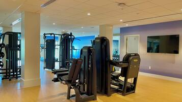 A gym with various exercise machines, a television on the wall, and a blue wall in the background.