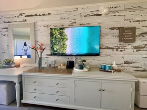 A modern living room with a flat-screen TV, a white cabinet with drawers, a mirror, and a decorative sign on the wall.