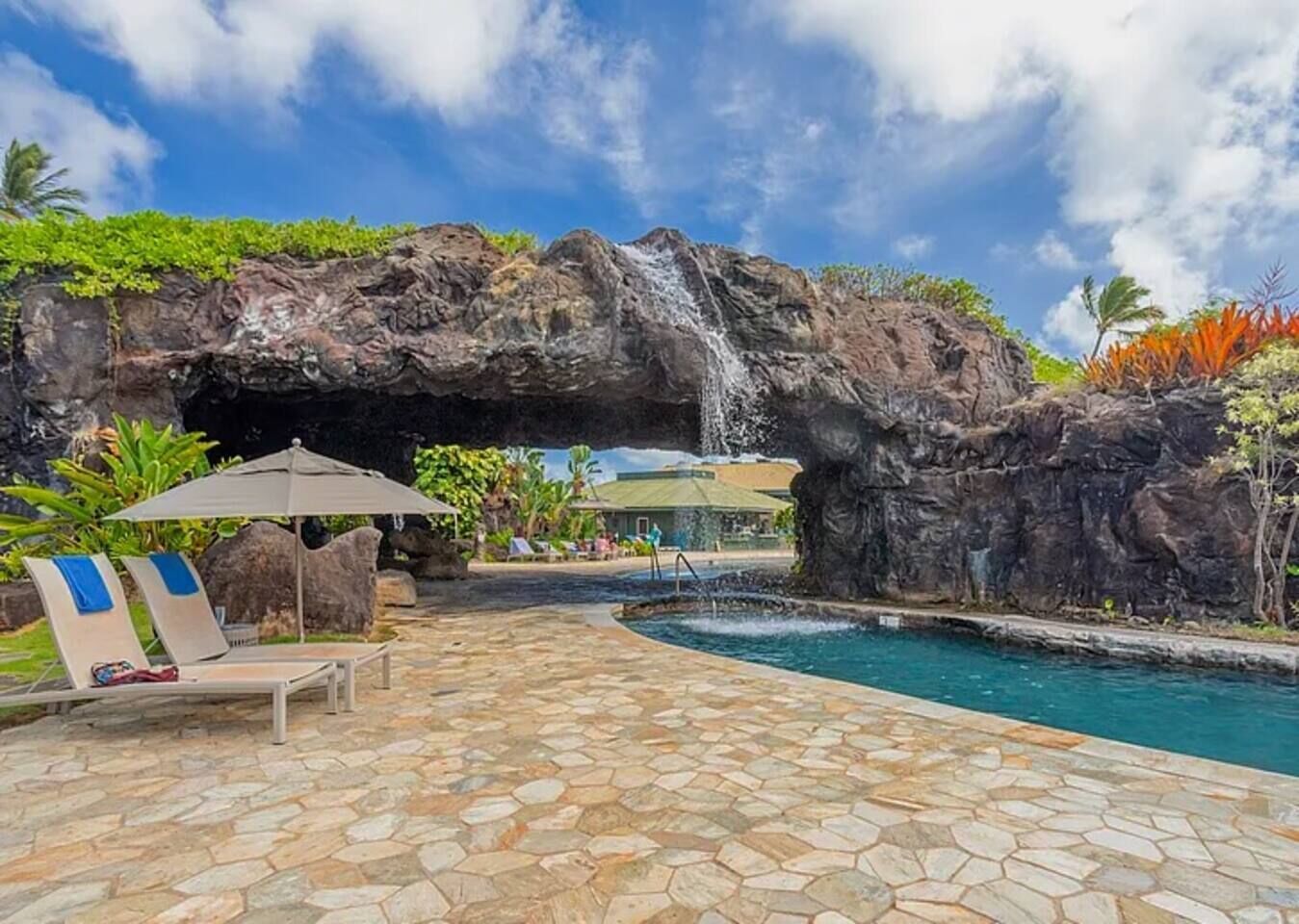 Un espace piscine agrémenté d’une cascade, de chaises longues et d’une terrasse dallée de pierres.