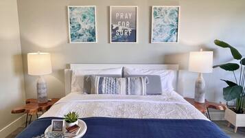 Une chambre à coucher bien rangée, avec un lit, deux tables de chevet, un plaid bleu, une petite plante et trois tableaux encadrés accrochés au mur.
