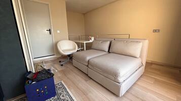 Una habitación pequeña amoblada con sofá, una silla, escritorio y puerta.