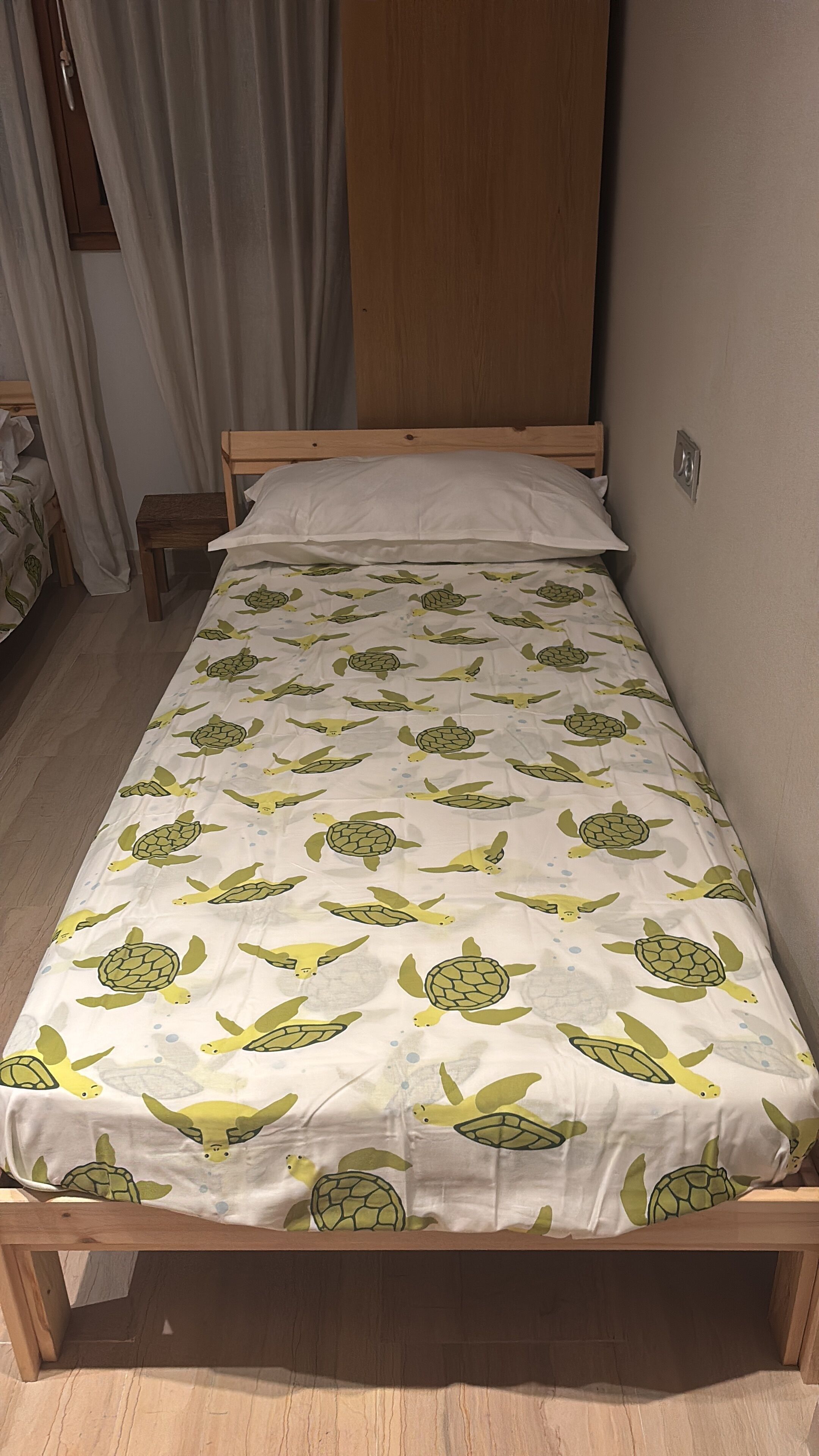 A single bed with a wooden frame and a white mattress with a sea turtle pattern.