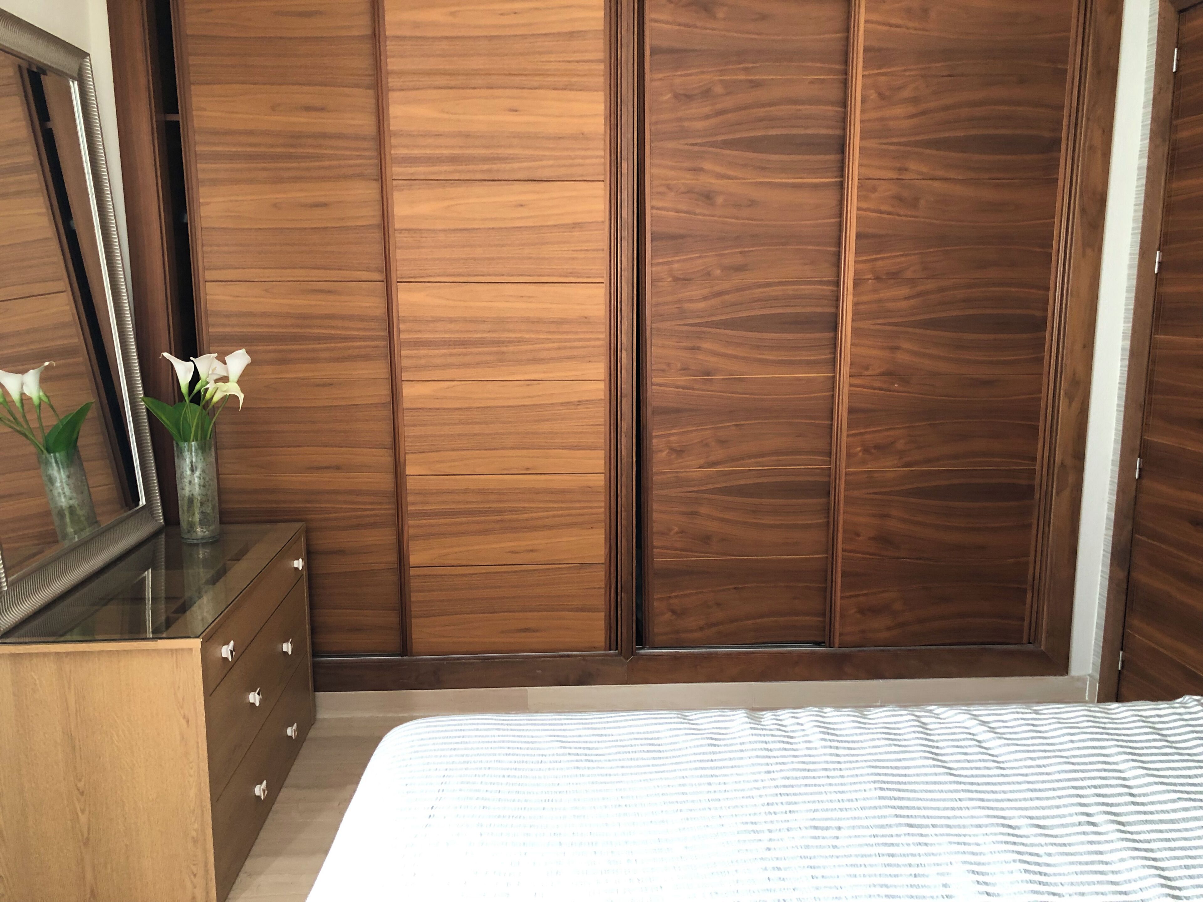 A bedroom with a wooden wardrobe, a dresser, and a bed with a striped bedspread.