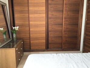 A bedroom with a wooden wardrobe, a dresser, and a bed with a striped bedspread.