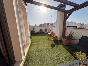 A rooftop terrace with artificial grass, potted plants, and outdoor furniture.