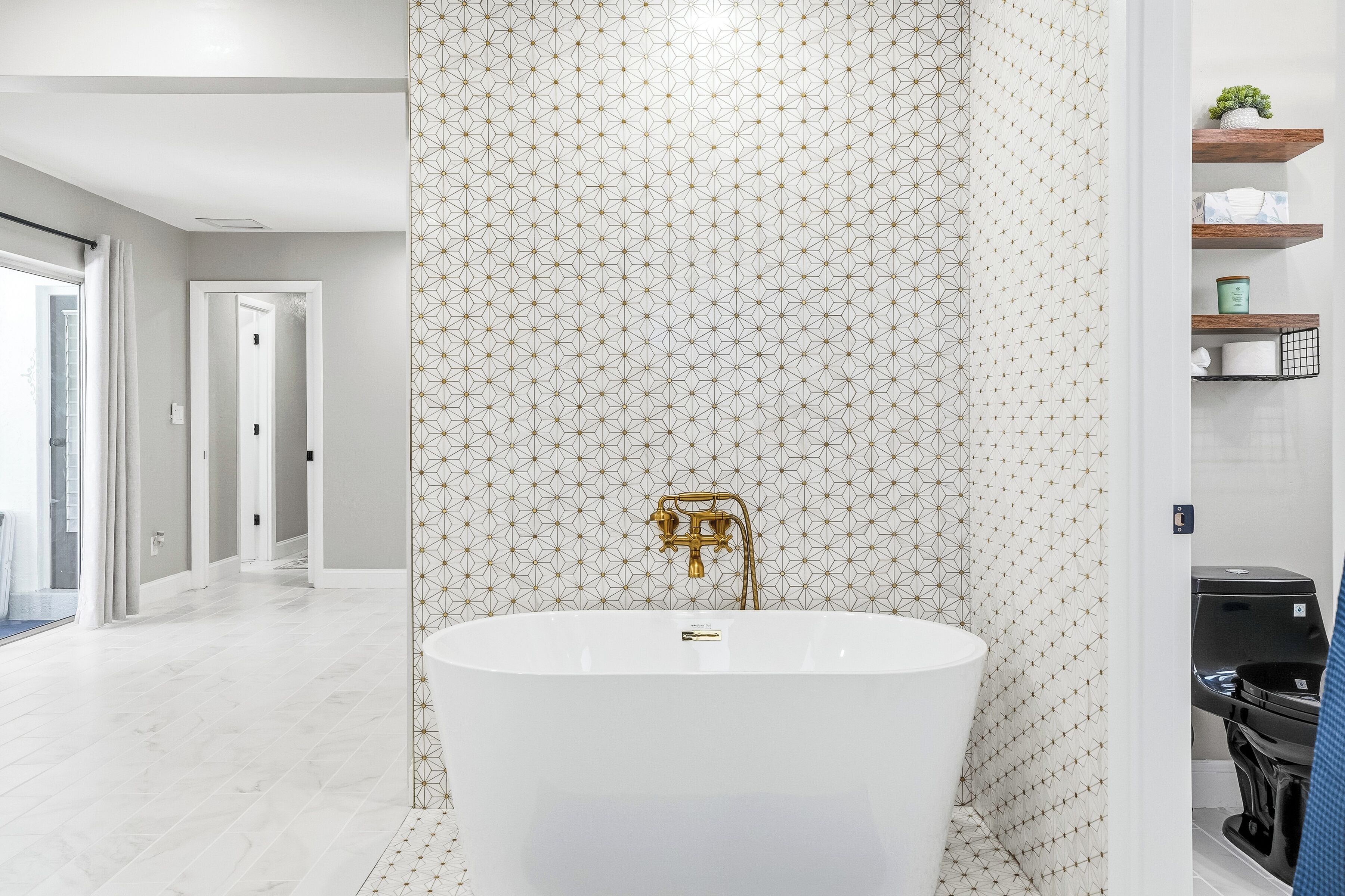 Un baño moderno con una bañera independiente, un cabezal de ducha dorado y un papel tapiz con diseño.