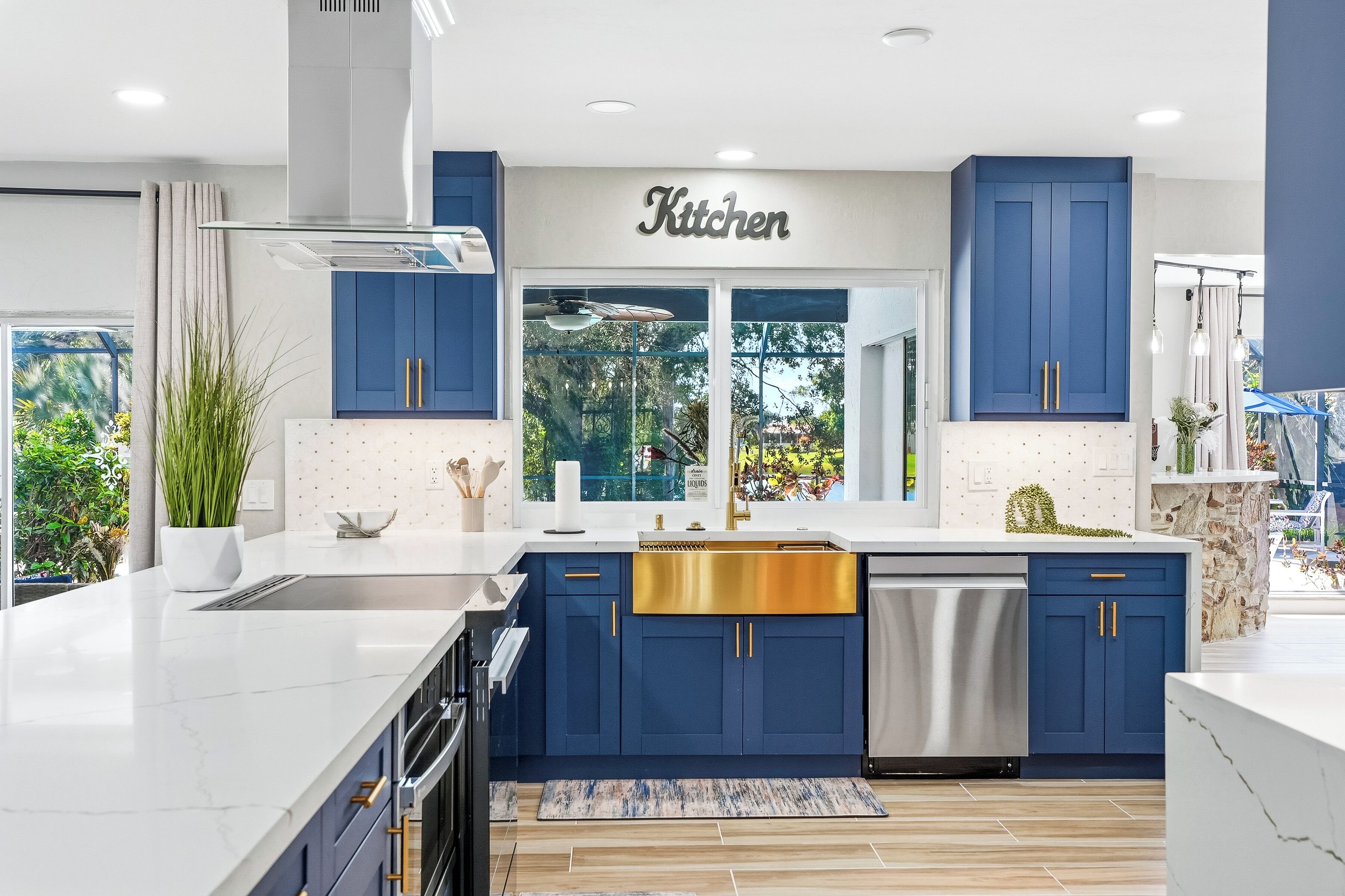 A modern kitchen with blue cabinets, a stainless steel sink, and a large window.