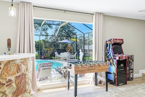 Um quarto com mesa de pebolim, mesa de bilhar e uma grande janela com vista para um jardim.
