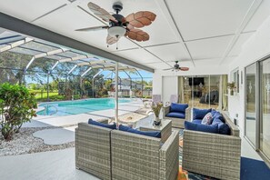 Un espacio exterior techado con piscina, mobiliario de mimbre y ventiladores de techo.