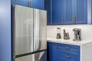 Une cuisine avec un réfrigérateur en acier inoxydable, des armoires bleues et un comptoir blanc.