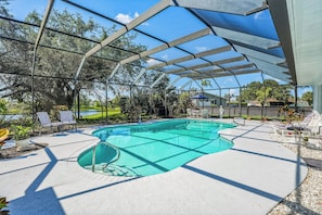 Piscina com estrutura de vidro, rodeada por espreguiçadeiras e vista para um lago.