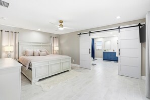 Une chambre avec un grand lit, un ventilateur de plafond et une salle de bain dotée d’un meuble-lavabo bleu.
