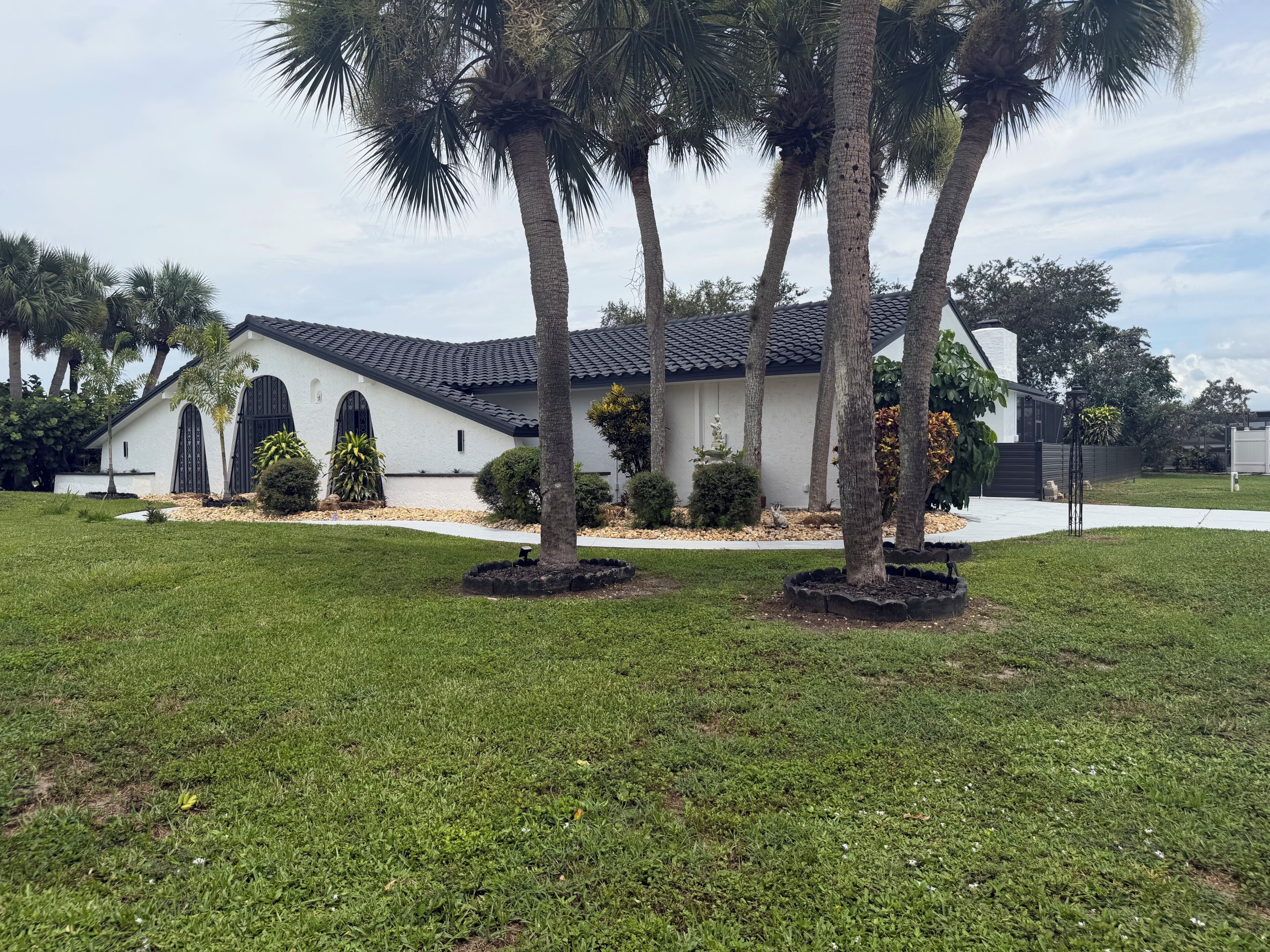 A white building with a black roof, surrounded by a well-maintained lawn and palm trees.
