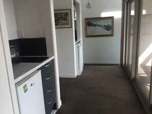 A narrow hallway with a kitchenette on the left, a refrigerator, and a painting on the wall. - Absolute beachfront in Waiwera (Waiwera)