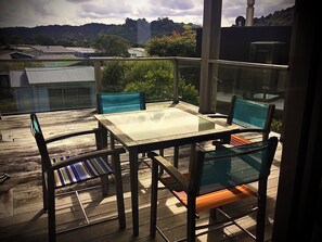 A balcony with a glass table and chairs, overlooking a residential area with houses and greenery. - Absolute beachfront in Waiwera (Waiwera)