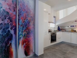 Eine moderne Küche mit weißen Schränken, einem Edelstahlbackofen und einem farbenfrohen, abstrakten Gemälde an der Wand.