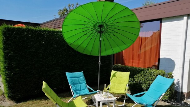 Un patio con quattro sedie da giardino, un tavolo e un ombrellone verde.
