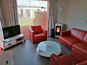 A living room with a TV, red leather sofas, a glass coffee table, and a fireplace. - Ein Bungalow in einem Ferienpark, ganz in der Nähe vom Meer by Interhome (Middelkerke)
