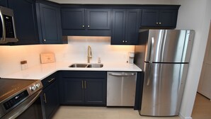A modern kitchen with dark blue cabinets, stainless steel appliances, and a white countertop. - Maritime Place B9 - Oceanfront in Garden City Beach (Garden City)