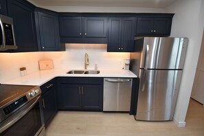 A modern kitchen with dark blue cabinets, stainless steel appliances, and a white countertop. - Maritime Place B9 - Oceanfront in Garden City Beach (Garden City)
