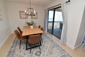 A dining area with a wooden table, six chairs, a vase with a plant, and a chandelier. - Maritime Place B9 - Oceanfront in Garden City Beach (Garden City)