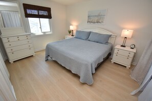 A bedroom with a bed, two bedside tables, a dresser, a window with blinds, and a painting on the wall. - Maritime Place B9 - Oceanfront in Garden City Beach (Garden City)