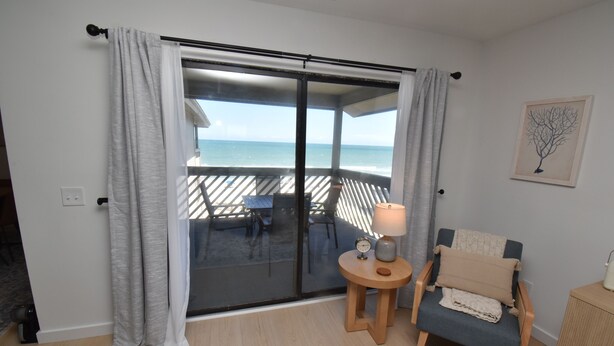 A room with a sliding glass door leading to a balcony with a view of the sea. There is a small round table with a lamp and a chair with a cushion. - Maritime Place B9 - Oceanfront in Garden City Beach (Garden City)