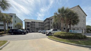 A parking lot with several cars, a building labeled 'Maritime Place,' and a sign with a logo. - Maritime Place B9 - Oceanfront in Garden City Beach (Garden City)