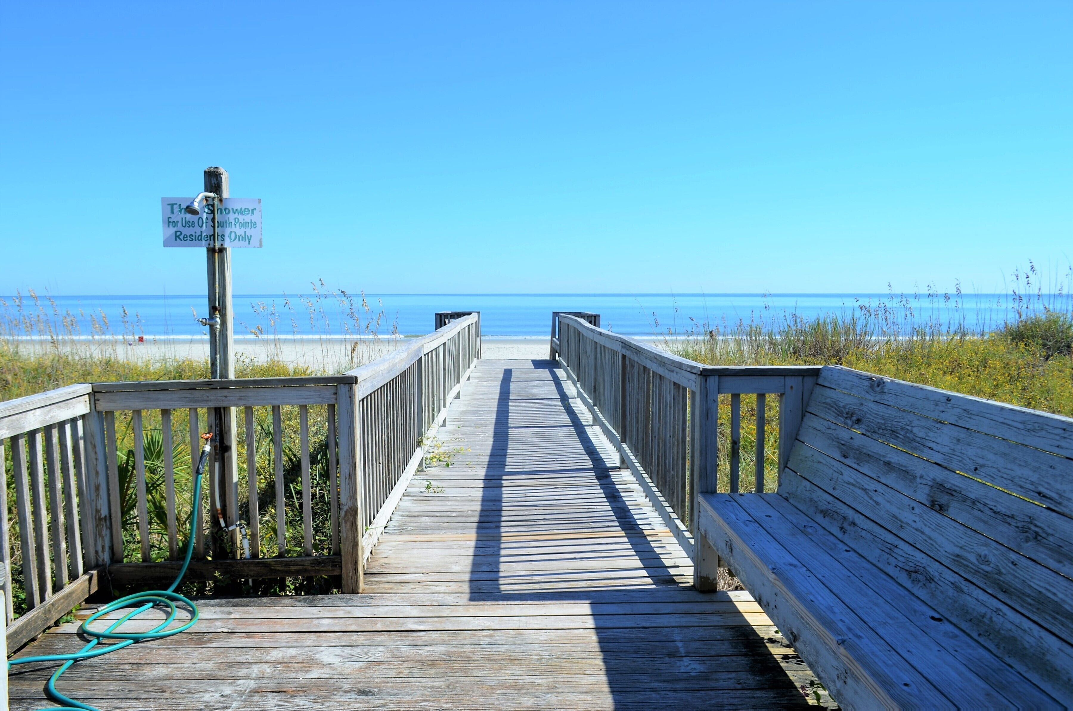 A wooden boardwalk leading to a beach with a sign indicating a shower for South Pointe residents only.