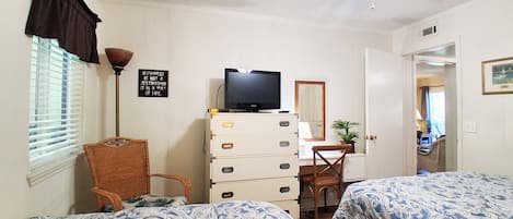 Et hotelværelse med to senge, et fjernsyn, en kommode, en stol og en ventilator.