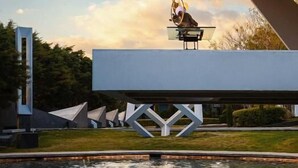Una estructura arquitectónica moderna con diseño geométrico, superficie reflectante y una fuente de agua debajo.