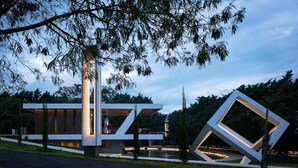 Un edificio moderno con un diseño geométrico original, rodeado de árboles y un sendero.