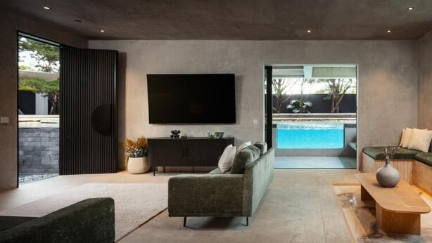 Una sala de estar moderna con una televisión de pantalla plana, un sofá, una mesa de centro y vista a una piscina.