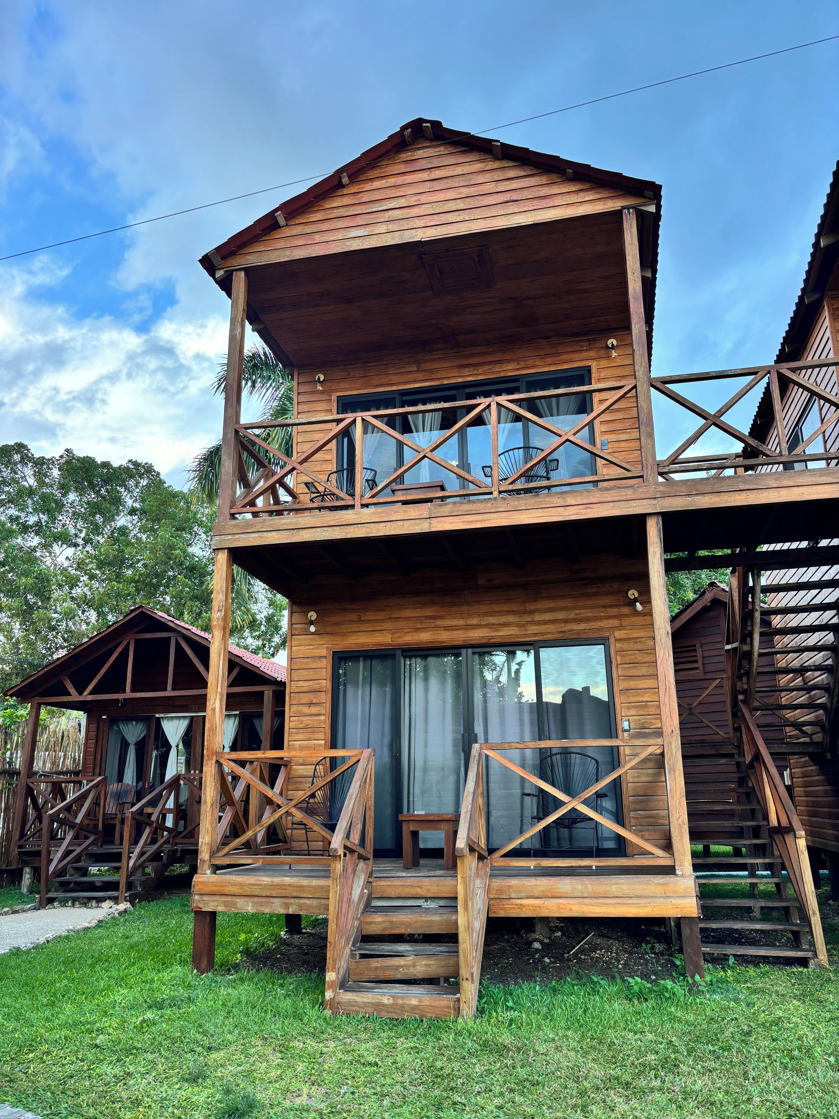 A wooden two-story cabin with a balcony, stairs, and a window with curtains.