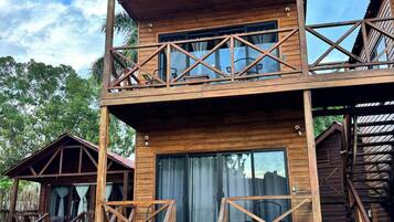A wooden two-story cabin with a balcony, stairs, and a window with curtains.