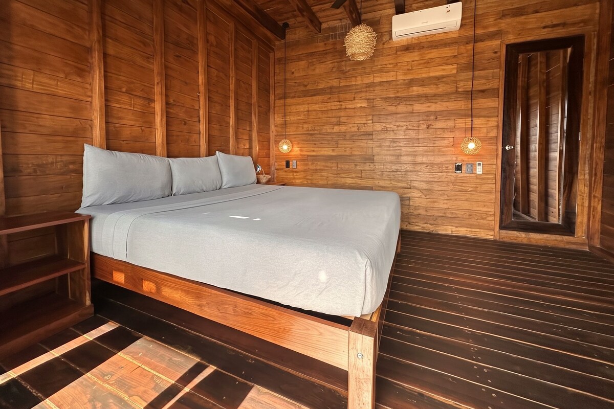 Un dormitorio tipo cabaña de madera con una cama, un ventilador de techo y un equipo de aire acondicionado de pared.