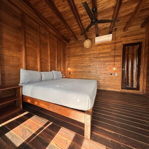 Un dormitorio tipo cabaña de madera con una cama, un ventilador de techo y un equipo de aire acondicionado de pared.