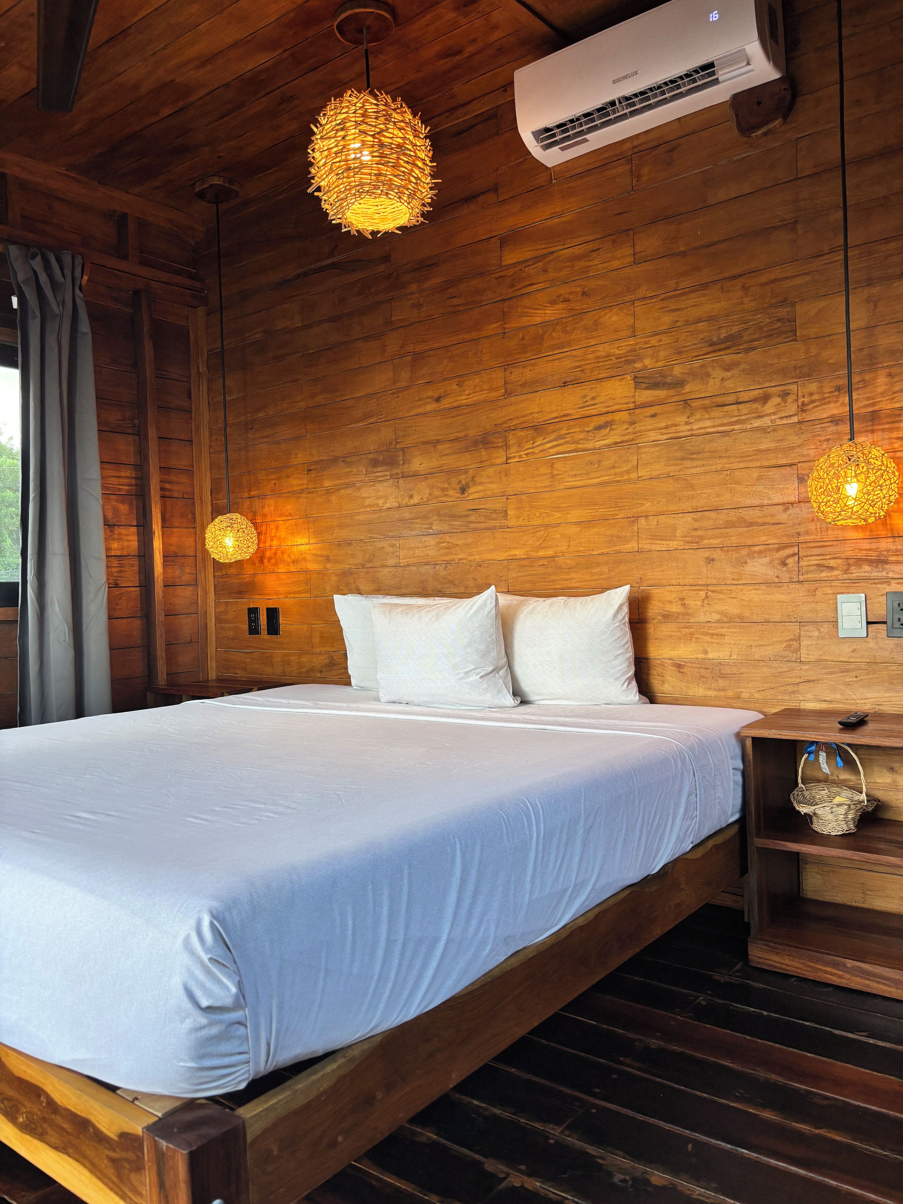 A wooden-paneled room with a bed, two wall-mounted air conditioners, and two hanging light fixtures.