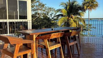 Una mesa de madera con bancos en un patio de ladrillo, con vista al mar y palmeras.
