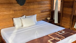 Una habitación de cabaña de madera con cama, un tapiz tejido en la pared y una ventana con cortinas.